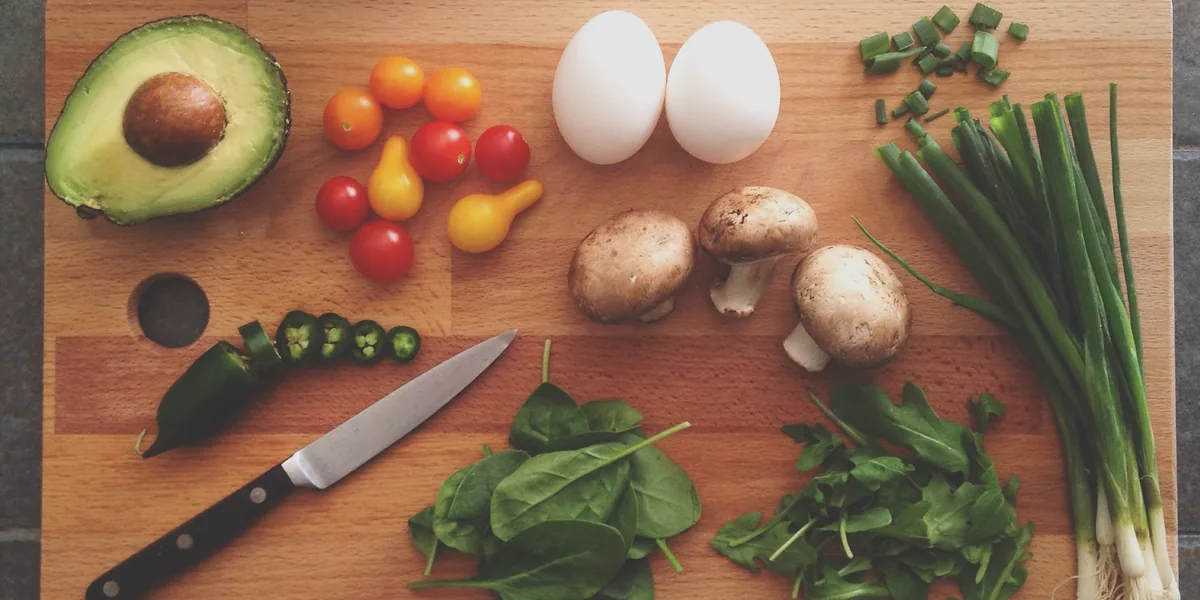 Schneidebrett mit Pilzen, Tomaten, Eiern, Spinat und Frühlingszwiebeln